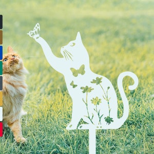 May include: White metal silhouette of a cat reaching up to a butterfly. The cat is decorated with flowers and butterflies. The silhouette is on a green grass background.