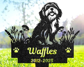 May include: Black metal garden stake featuring a silhouette of a dog with the name "Waffles" and the years 2012-2025. The dog is sitting in a field of flowers and grass, with paw prints on either side of the name.
