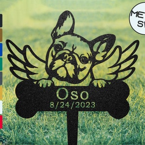 May include: Black metal garden memorial with a French Bulldog with wings holding a bone shaped plaque with the name "Oso" and the date "8/24/2023".