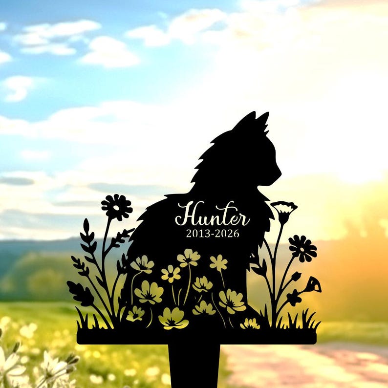 May include: A black metal garden stake featuring a silhouette of a cat sitting among flowers. The cat's body is engraved with the name Hunter and the years 2013-2026 in a white script and sans-serif font, set against a bright outdoor background.