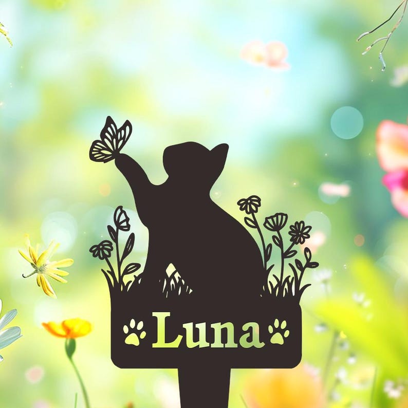 May include: A black metal garden stake featuring a silhouette of a cat reaching toward a butterfly, surrounded by floral stems. The rectangular base displays the name Luna in a serif font, flanked by two small paw print icons on each side.