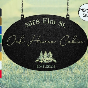 Puede incluir: Letrero metálico ovalado negro con el texto "5678 Elm St. Oak Haven Cabin" en una fuente decorativa. El letrero incluye un gráfico de bosque y ciervo y "EST.2024". El letrero cuelga de cadenas.
