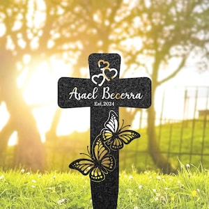 May include: Black metal cross with a butterfly design and the text "Asael Becerra Est. 2024" on a black background.