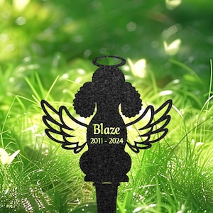 Könnte beinhalten: Schwarze Metallsilhouette eines Pudels mit Engelsflügeln und einem Heiligenschein. Die Silhouette befindet sich auf einem Pfahl und trägt den Text "Blaze 2011-2024" auf der Vorderseite. Die Silhouette befindet sich vor einem grünen Gras Hintergrund.