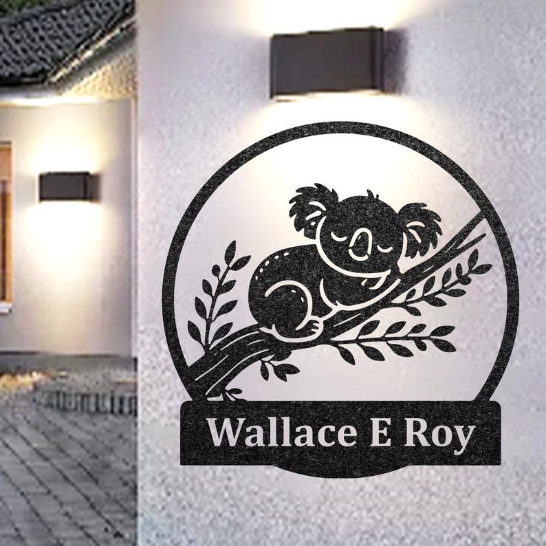 Pode incluir: Um sinal de metal preto com a silhueta de um coala dormindo em um galho. O sinal tem uma moldura circular e uma placa retangular com o nome "Wallace E Roy".