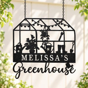 May include: A black metal hanging sign shaped like a greenhouse, featuring cutouts of a watering can, potted plants, boots, and a shovel. The text reads MELISSA'S Greenhouse in a mix of block and script fonts, suspended by two black chains.