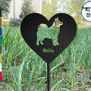 Puede incluir: Estaca de jard&iacute;n de metal negro en forma de coraz&oacute;n con una silueta de un perro y el nombre "Bella" inscrito debajo. La estaca est&aacute; en un &aacute;rea cubierta de hierba.