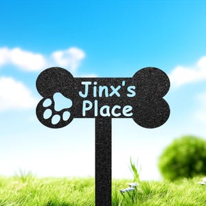 May include: Black metal bone-shaped sign with a paw print and the text "Jinx's Place" on a green grassy background.