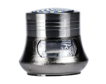 May include: A metallic gray herb grinder with a textured finish. The top features a colorful, patterned design. The grinder has a clear window and a unique, rounded shape.