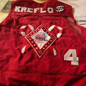 May include: Red mesh vest with a white embroidered patch that says "KREFLO$" and a white number "4" on the back. The patch features a red car, palm trees, and candy canes.