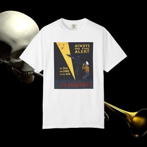 May include: A white t-shirt featuring a graphic print of a vintage U.S. Marines recruitment poster. The design shows a soldier using a telescope, a yellow searchlight beam, and the text: Always on the alert, at sea, on land, in the air, U.S. Marines.
