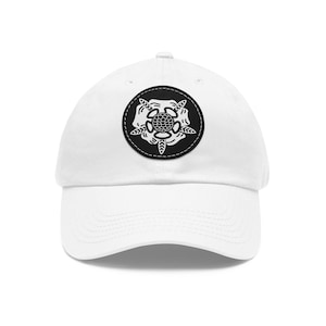 May include: White baseball cap with a black and white embroidered patch of a stylized flower design.