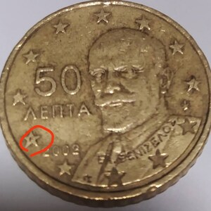 Op de afbeelding: Een gouden 50 lepta munt uit Griekenland met een portret van koning George I. De munt heeft een stervormig ontwerp rond de rand en het jaar 2002 is zichtbaar.