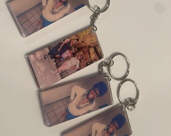 May include: Four rectangular photo keychains with silver key rings. Each keychain features a different photo of a person or people. The photos are printed on clear plastic.