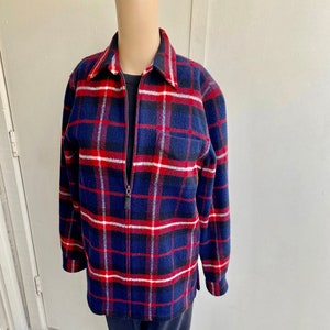 Puede incluir: Una camisa de franela a cuadros azules, rojos y blancos con cierre de cremallera. La camisa tiene un corte holgado y mangas largas.