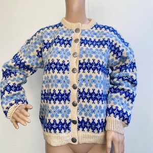 Könnte beinhalten: Ein cremefarbener Cardigan mit einem blauen und hellblauen geometrischen Muster. Der Cardigan hat einen Knopfschließe und lange Ärmel.