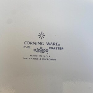 Może przedstawiać: Biały garnek Corning Ware z czarnym wzorem kwiatowym i nadrukiem "Corning Ware" oraz "P-21 Roaster" na spodzie. Na spodzie znajduje się r&oacute;wnież napis "Made in U.S.A. for Range & Microwave".