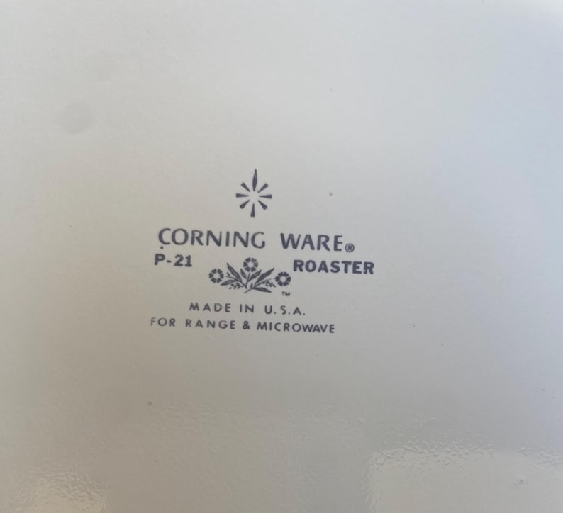 Może przedstawiać: Biały garnek Corning Ware z czarnym wzorem kwiatowym i nadrukiem "Corning Ware" oraz "P-21 Roaster" na spodzie. Na spodzie znajduje się r&oacute;wnież napis "Made in U.S.A. for Range & Microwave".