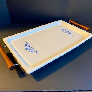 Könnte beinhalten: Ein weißes Keramik-Serviertablett mit blauen Blumenmustern und Holzgriffen. Das Tablett hat eine rechteckige Form und ist perfekt zum Servieren von Snacks oder Getränken.