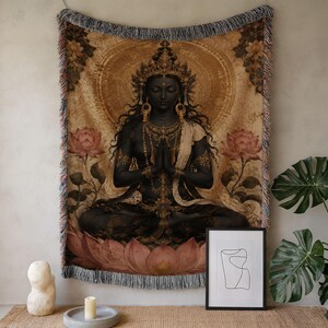 May include: A rectangular woven wall tapestry featuring a dark-skinned figure in a meditative pose with hands pressed together. The figure wears ornate gold jewelry and a crown, surrounded by pink lotus flowers against a golden, circular background.