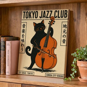Könnte beinhalten: Ein rechteckiger Leinwanddruck mit einer schwarzen Katze, die einen orangefarbenen Kontrabass spielt. Der Text lautet TOKYO JAZZ CLUB, 131-0045 TOKYO und SUMIDA CITY-OSHIAGE, ergänzt durch japanische Schriftzeichen auf cremefarbenem Grund.