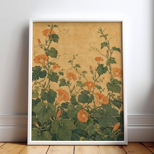 May include: A framed wall art print featuring a botanical illustration of orange morning glory flowers with green leaves and winding vines set against a textured, golden-yellow background. The artwork is enclosed in a simple white frame.