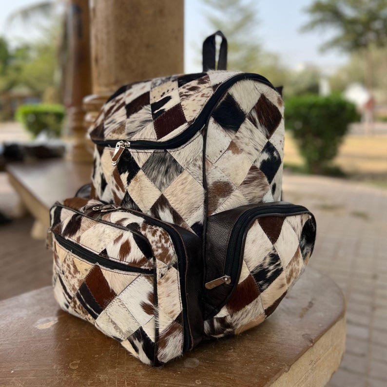 May include: A patchwork backpack with matching side pouches. The bag features a geometric pattern of brown, black, and cream-colored leather squares. The backpack has a black handle and zippers.