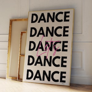 Op de afbeelding: Een ingelijste kunstdruk met het woord "DANCE" vijf keer herhaald in vette zwarte letters, met "Lets" in roze cursief in het midden. De print heeft een gouden lijst en leunt tegen een witte muur en een houten vloer.