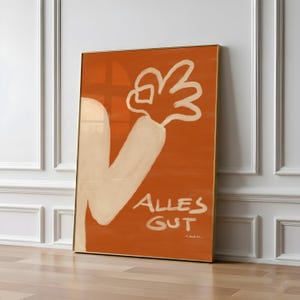 May include: Orange framed art print featuring a white arm and hand making an 'okay' gesture. The words 'Alles Gut' are written in white script. The artwork has a minimalist style and is displayed against a white wall.