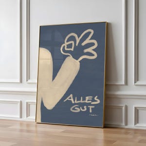 May include: A framed wall art print featuring a dark blue background with a beige, hand-drawn illustration of an arm and a hand making an okay gesture. The text ALLES GUT is written in a matching beige, brush-stroke style font below the hand.