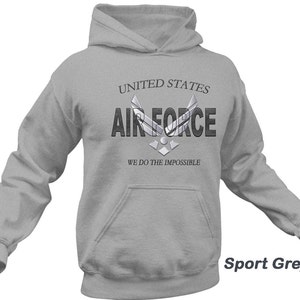 Może przedstawiać: Szara bluza z kapturem z nadrukiem "United States Air Force" i logo Sił Powietrznych na przodzie. Pod logo znajduje się napis "We do the impossible". Bluza jest oznaczona jako "Sport Grey".