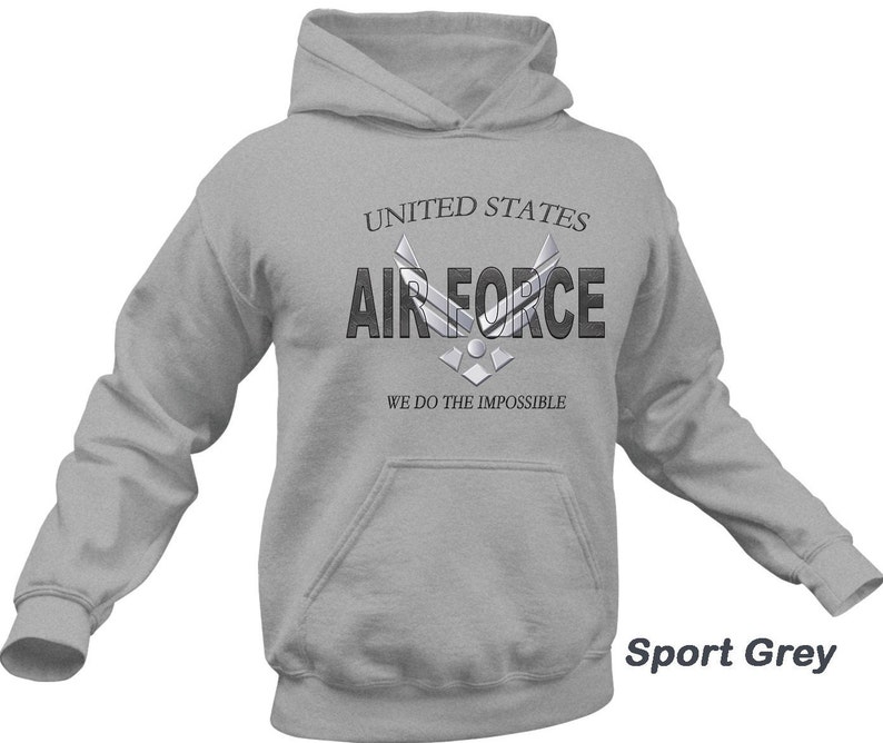 Może przedstawiać: Szara bluza z kapturem z nadrukiem "United States Air Force" i logo Sił Powietrznych na przodzie. Pod logo znajduje się napis "We do the impossible". Bluza jest oznaczona jako "Sport Grey".