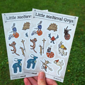 May include: Two identical sticker sheets titled Little Medieval Guys featuring various whimsical illustrations of anthropomorphic animals and creatures in a medieval style, including rabbits, snails, and hybrid beings, with the text Radical rascal at the bottom.