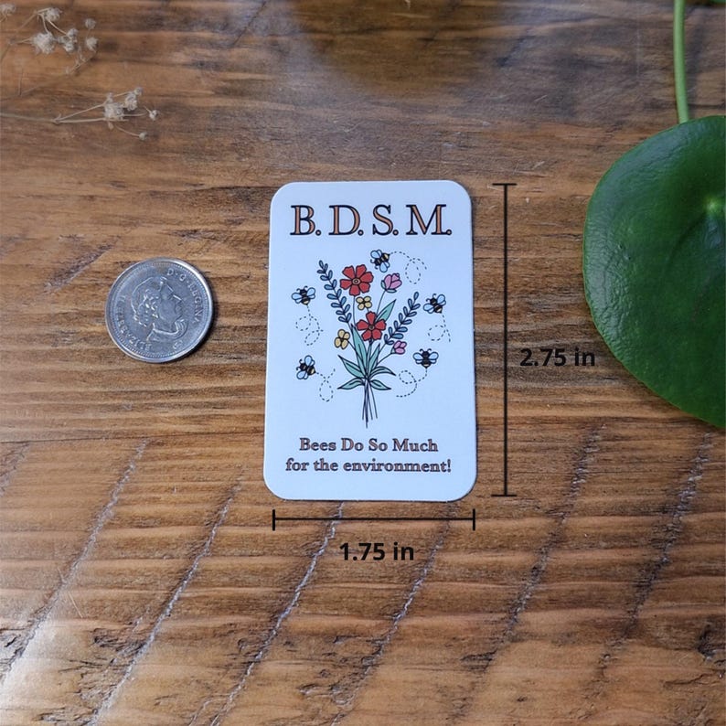 May include: A rectangular white sticker featuring a bouquet of red, yellow, and blue flowers surrounded by small bees. The text reads B.D.S.M. and Bees Do So Much for the environment! The sticker measures 2.75 inches in height and 1.75 inches in width.