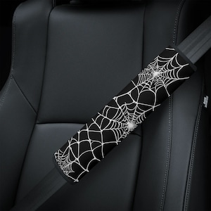 May include: Black and white spiderweb patterned car seatbelt cover. The cover is made of a soft, comfortable fabric and is designed to protect your seatbelt from wear and tear.