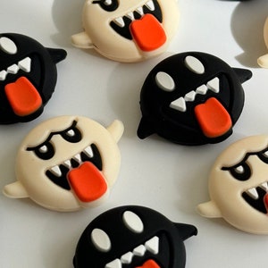 May include: A set of eight black and white ghost-shaped silicone charms with a cartoonish expression, including a tongue sticking out and teeth.