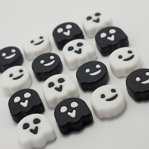 May include: A collection of black and white ghost-shaped charms with different facial expressions. The charms are made of silicone and have a smooth, glossy finish.
