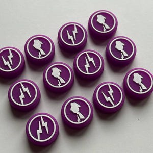 May include: A collection of purple, circular buttons with white graphic designs. Each button features a white lightning bolt and a silhouette of a person. The buttons are arranged on a white surface.