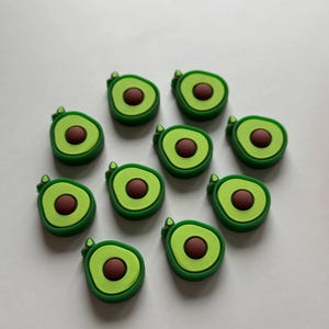 May include: Ten green and brown avocado-shaped charms with a brown pit inside. The charms are made of a soft, flexible material.