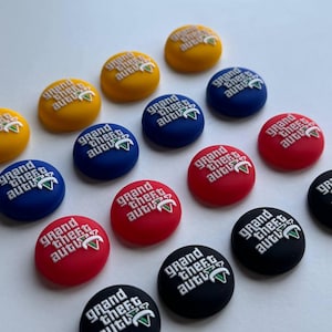 May include: A collection of colorful, round buttons with the text "Grand Theft Auto" in white. The buttons are in various colors, including yellow, blue, red, and black. Each button has a small green triangle.
