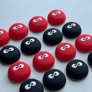May include: A collection of red and black round objects, each featuring a pair of white, cartoon-style eyes. The objects are arranged on a white surface. The red objects are a vibrant, solid color, while the black ones offer a contrasting dark hue.