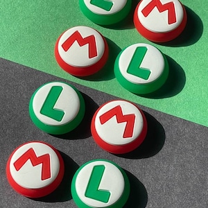 May include: A collection of round, colorful buttons featuring the letters "L" and "M". The buttons have a white center with either a green "L" or a red "M". The outer ring of the buttons is either green or red. The background is a mix of green and gray.