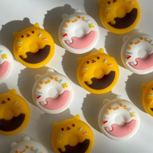 May include: Assortment of colorful donut-shaped resin charms with cute animal faces. The charms are yellow, white, and pink with brown and white details.