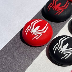 May include: Four round silicone controller caps with a spider design. Two caps are black with a white spider and two caps are red with a white spider.
