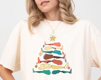 May include: A white t-shirt with a colorful Christmas tree design made of legs. The tree is decorated with ornaments and a star on top. The shirt is available in ivory.