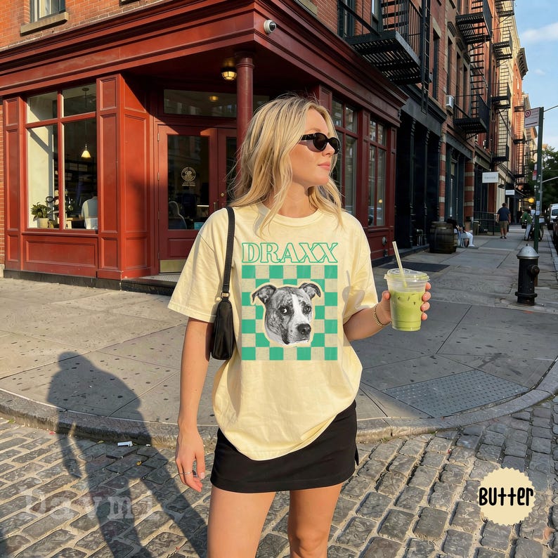 Peut inclure: Un t-shirt &agrave; manches courtes jaune p&acirc;le avec un motif &agrave; damier vert et beige, un portrait de chien en noir et blanc et le texte DRAXX imprim&eacute; en vert. Le t-shirt pr&eacute;sente une encolure ronde et une coupe ample et d&eacute;contract&eacute;e.