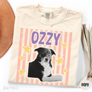 Peut inclure: Un t-shirt &agrave; manches courtes couleur ivoire avec une impression graphique repr&eacute;sentant un chien noir et blanc. Au-dessus du chien, le nom OZZY est imprim&eacute; en lettres violettes. Le fond du motif pr&eacute;sente des rayures p&ecirc;che et des &eacute;toiles jaunes.