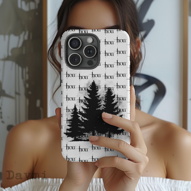 May include: White phone case with a black tree silhouette design. The case has a repeating pattern of the word "hoa" in black. The phone case is held in front of a person.