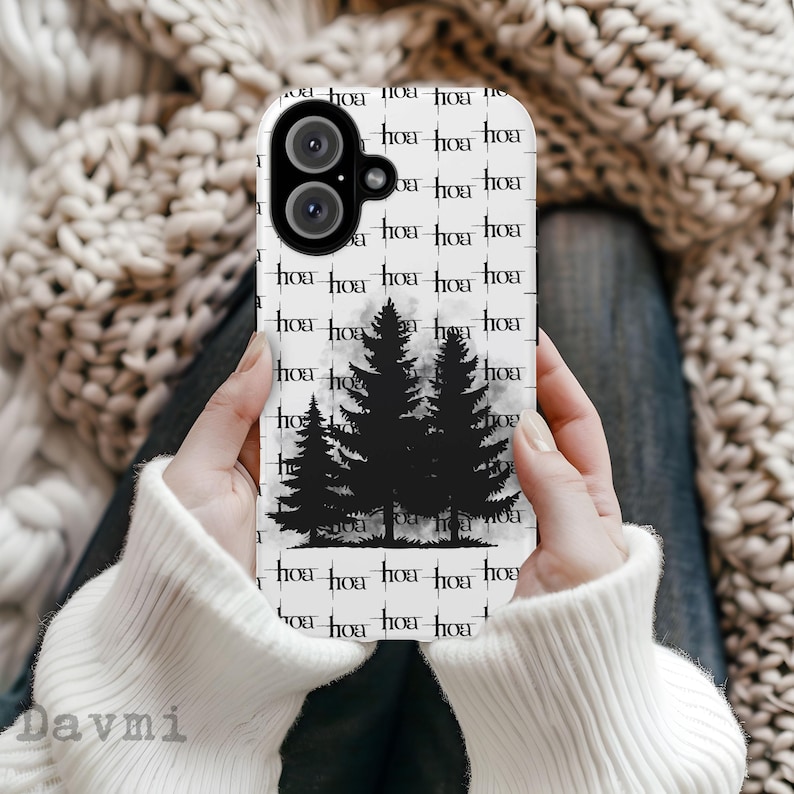 May include: White phone case featuring a black silhouette of three pine trees against a misty background. The case has a repeating pattern of the word "hoa" in a black, stylized font. The phone case is held in a person's hands.