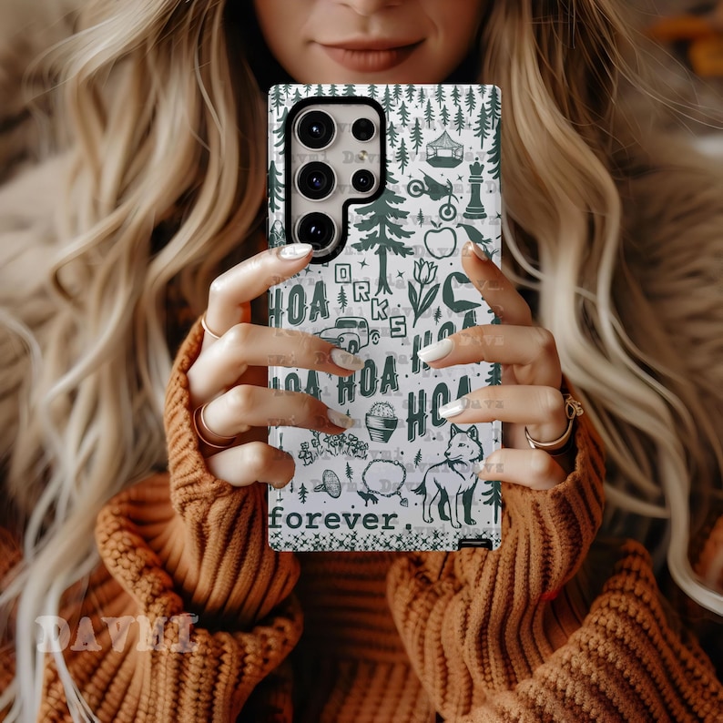 May include: A white phone case with a green forest-themed pattern, including trees, a wolf, and the word "forever." The case is held up by a person wearing a brown sweater.